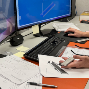 An engineer works intently at a computer station, using CAD software to transform concepts into detailed engineering blueprints. The focus is on the screen displaying complex diagrams, illustrating the precision and expertise involved in the engineering process.