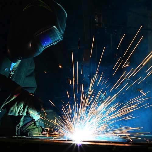 A skilled worker in protective gear performs welding in a fabrication workshop. Sparks fly as the worker meticulously joins metal parts, showcasing the precision and craftsmanship involved in the fabrication process.